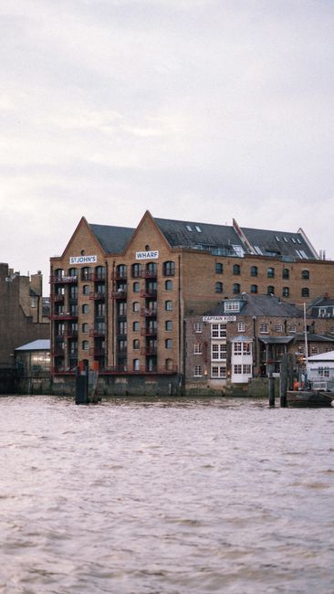 A row of modern high-rise residential and commercial buildings along the riverbank, with large glass windows and concrete facades. The buildings vary in height and architectural style, with some featu