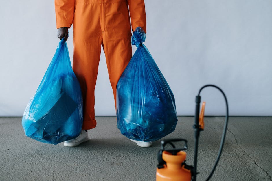 A blue recycling bin is positioned upright on a concrete pavement beside a white mobile delivery or removal truck with a large white cargo area, which has visible door hinges and a vertical metal stri